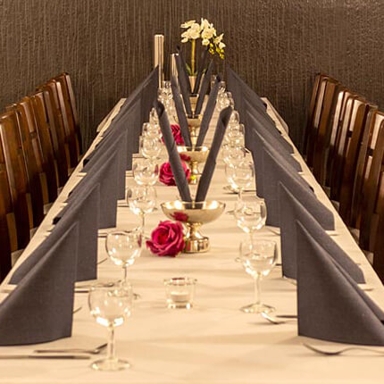 Elegant gedeckter Tisch mir grauen Servietten, weißer Tischdecke und roten Rosen für Eventraummietung in Hamburg.